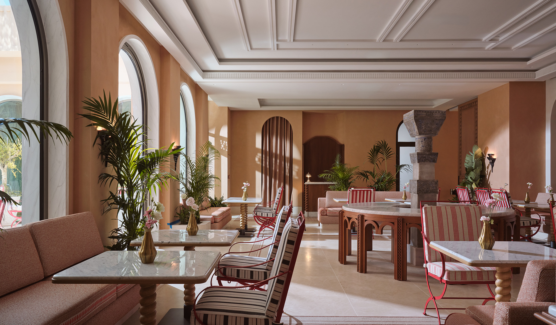 Byzantino Grande Brasserie at Conrad Athens The Ilisian, with marble dining tables, striped chairs, upholstered banquettes and tall arched windows overlooking the greenery