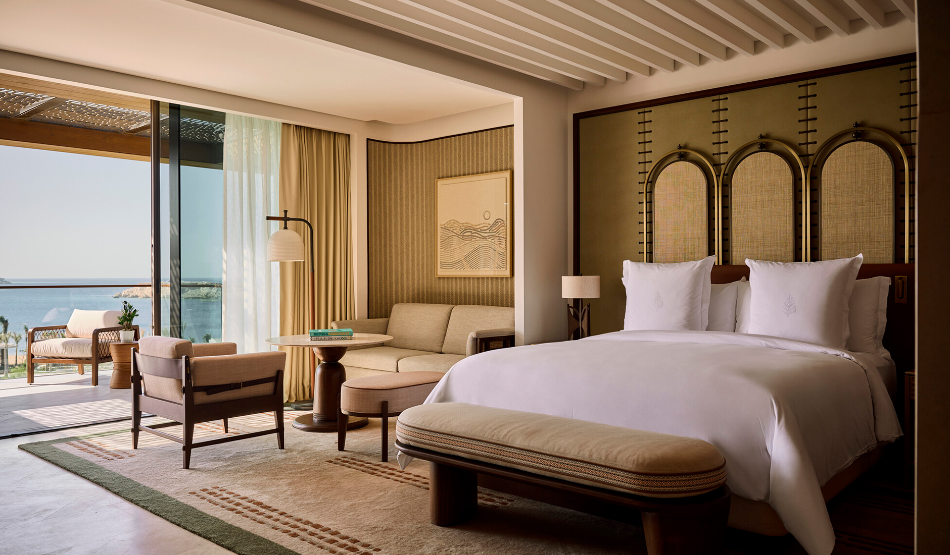 Opulent bedroom interior of a luxury suite at Four Seasons Resort AMAALA at Triple Bay, featuring a plush king-size bed facing floor-to-ceiling glass walls with panoramic Red Sea views.