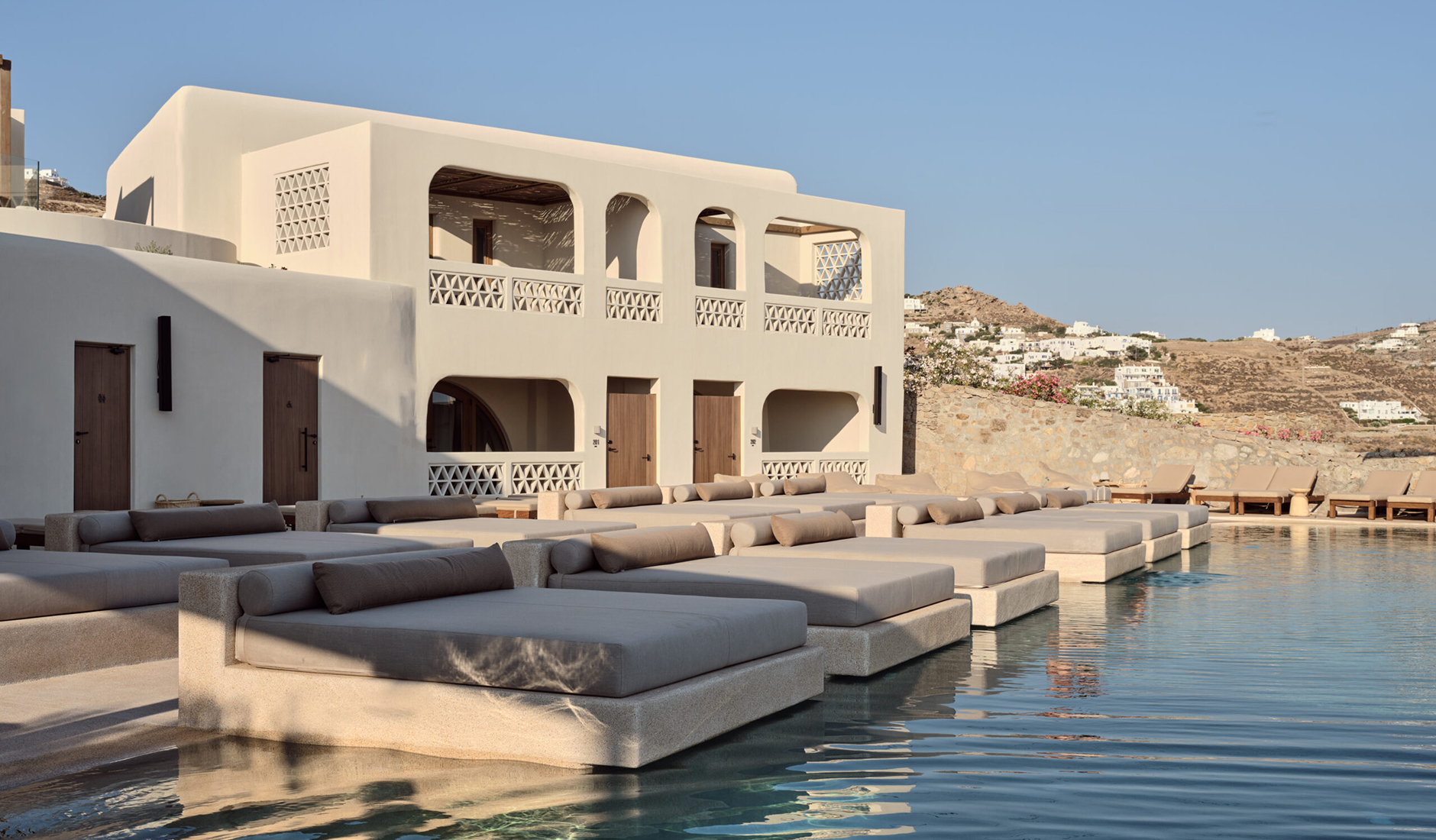 Minimalist white Cycladic architecture at Omeon, ranked among the best luxury hotels in Mykonos, featuring an infinity pool with Aegean Sea views.
