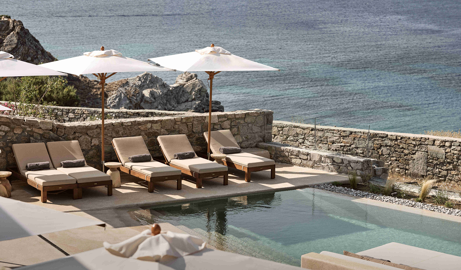 Spectacular main infinity swimming pool at Omeon Mykonos, seamlessly cascading down the hillside towards the deep-blue Aegean horizon.