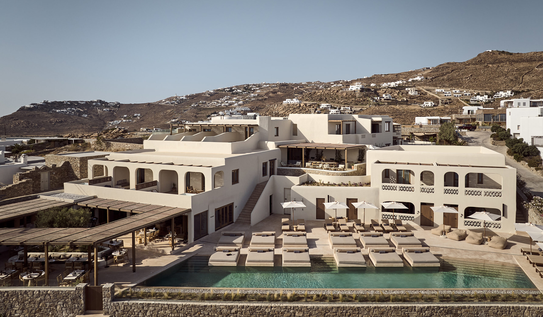 Minimalist white Cycladic architecture at Omeon, ranked among the best luxury hotels in Mykonos, featuring an infinity pool with Aegean Sea views